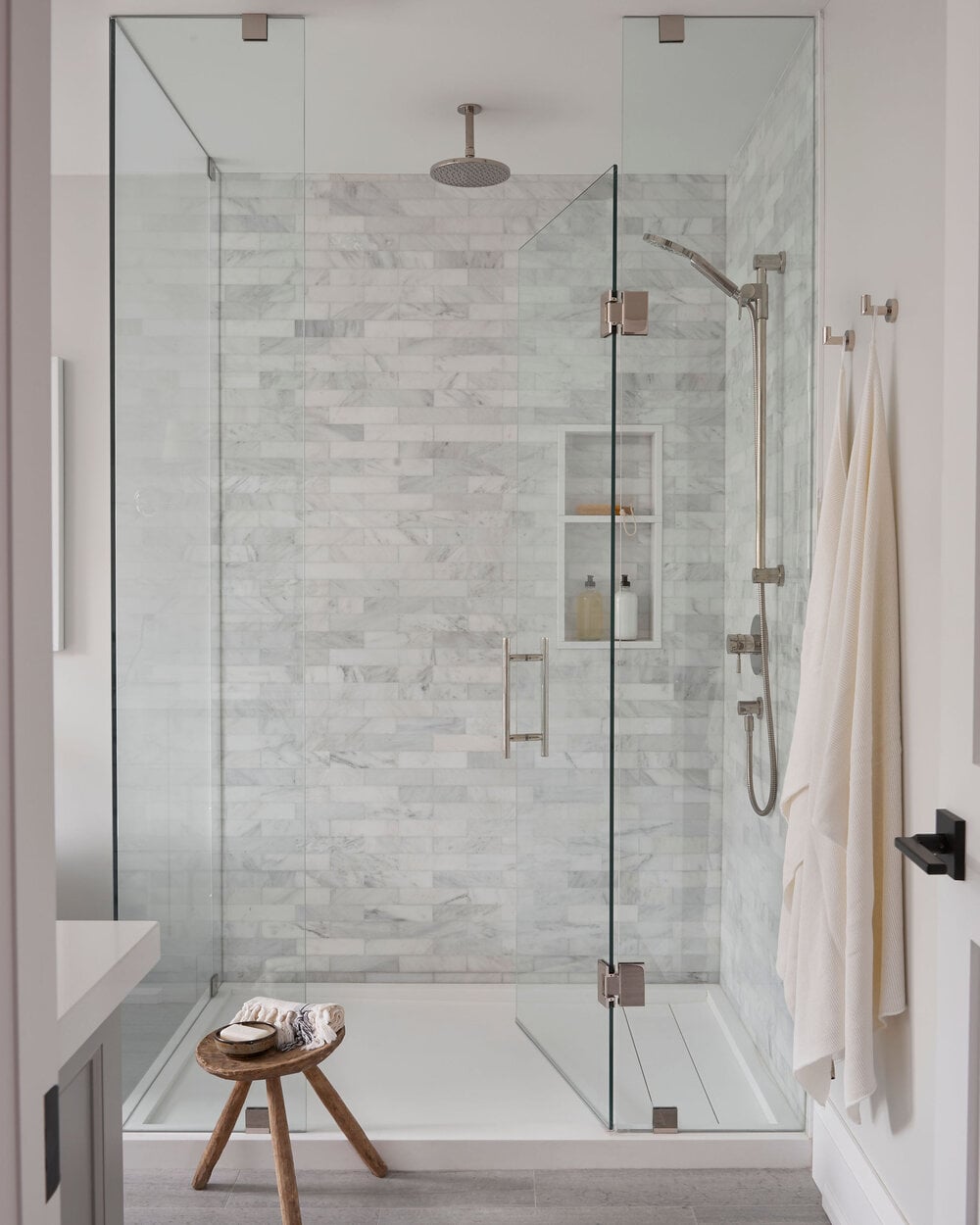 Contemporary shower space with wall-mounted nickel shower head and controls, complemented by clear glass doors.